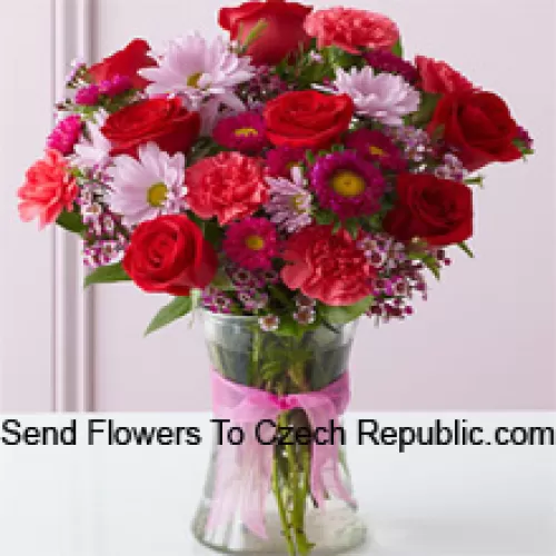 Roses rouges, oeillets rouges et autres fleurs assorties disposées magnifiquement dans un vase en verre